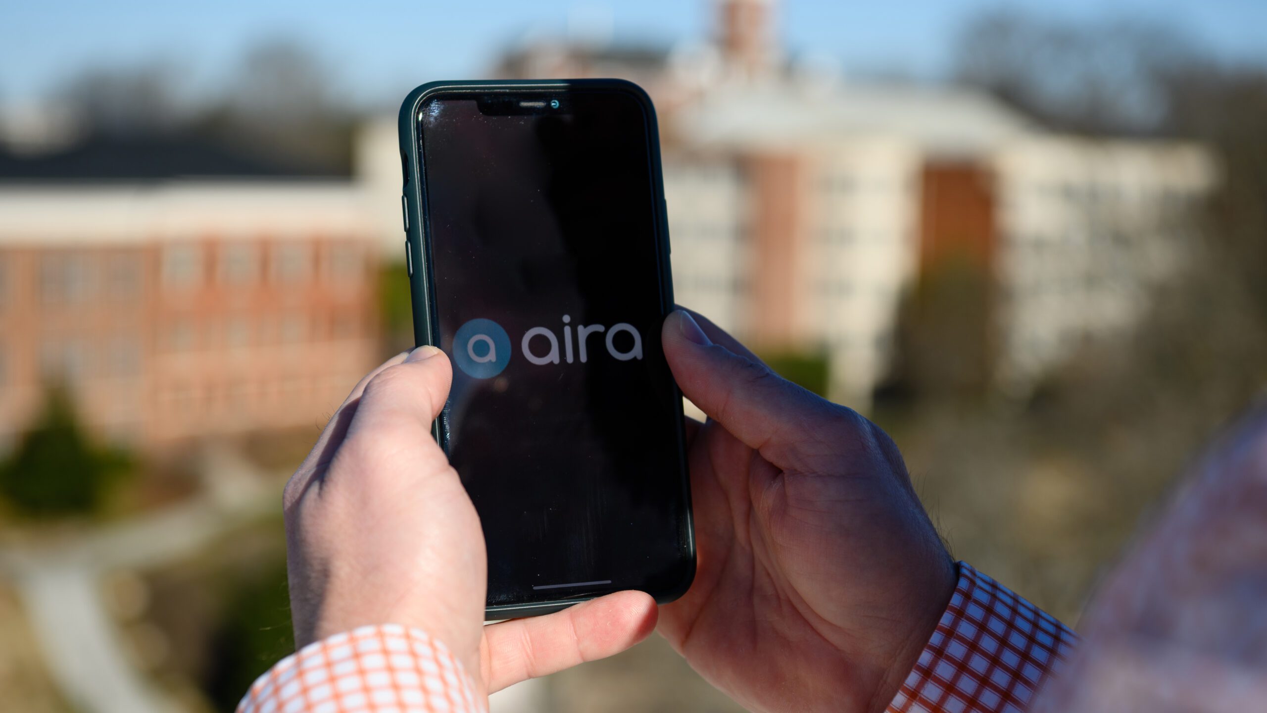 A man's hands holding an iPhone with an Aira logo