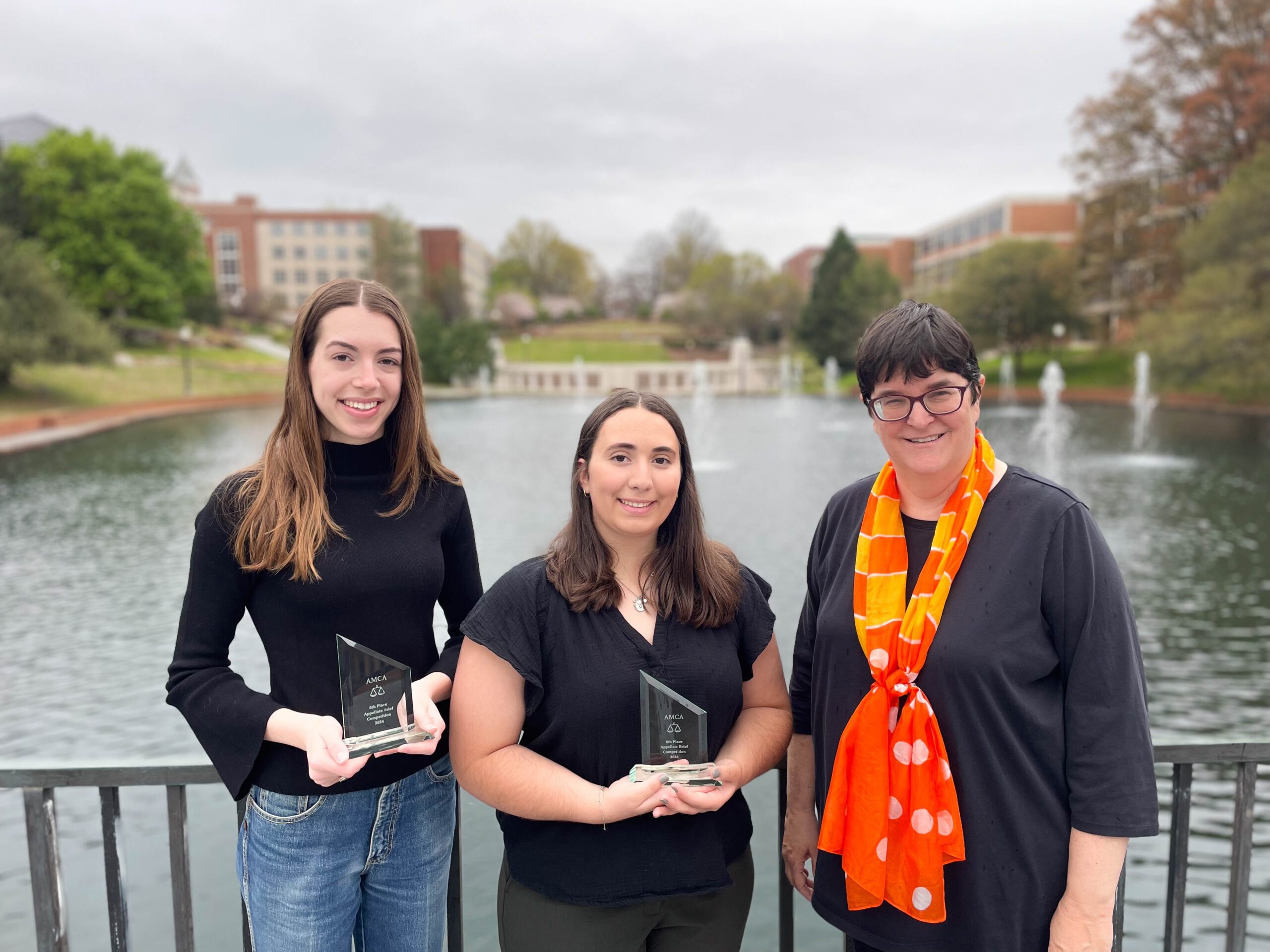 Caroline Morgan (left), Teresa Ribeiro (middle) and Cary Berkeley Kaye pose for a picture in front of the reflection pond on Clemson University's main campus. The weather is gloomy.