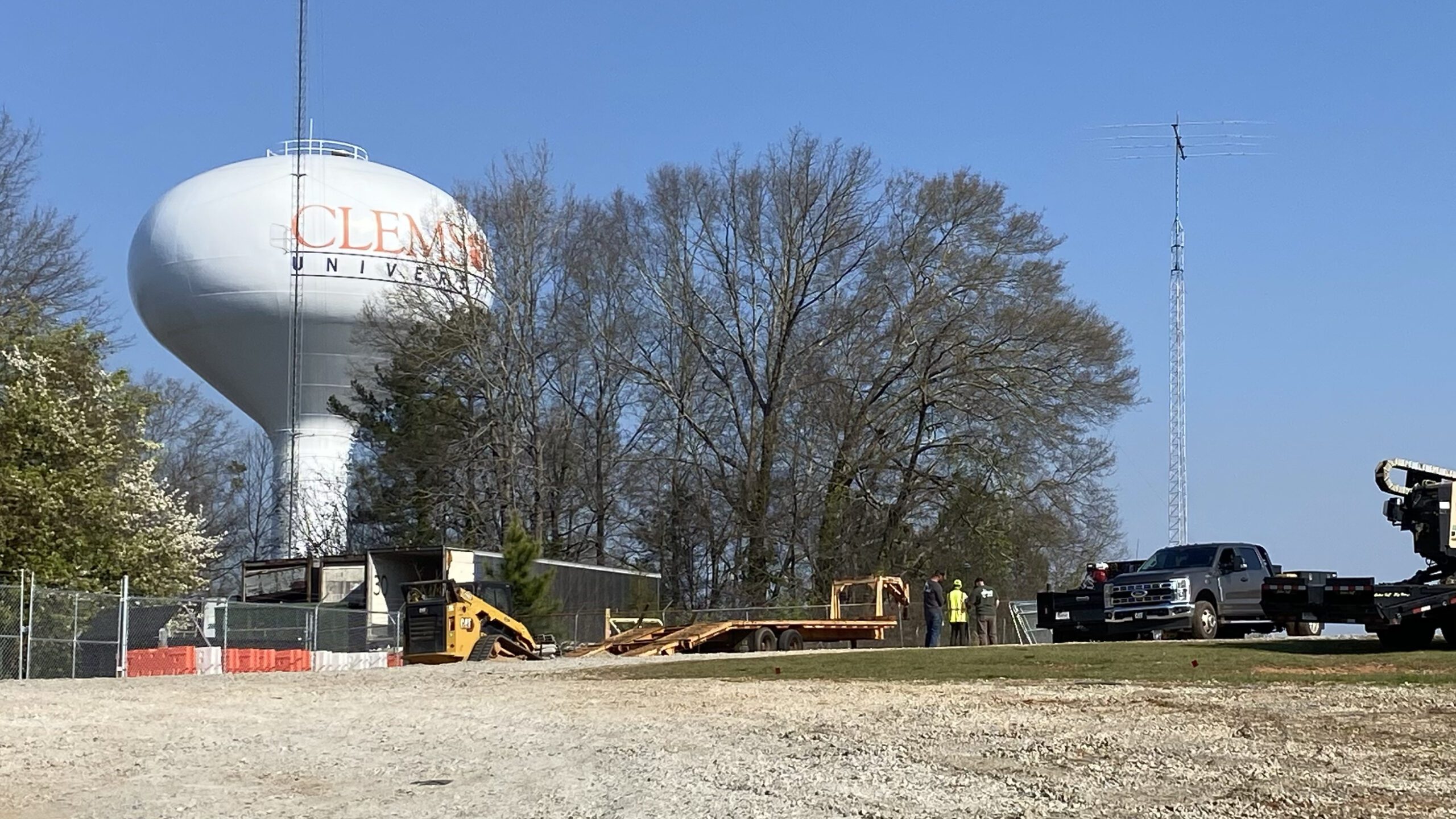 Construction vehicles on a gravel lot in front of a Clemson-branded water tower