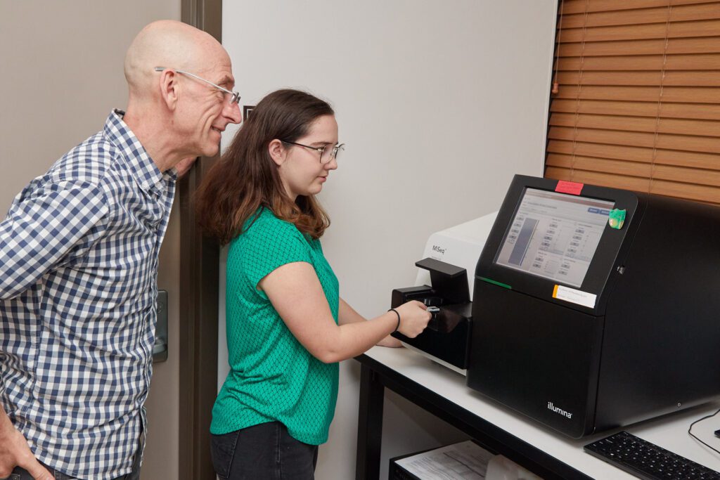 Man watches a woman wearing a green shirt insert a sample into a sequencing machine.