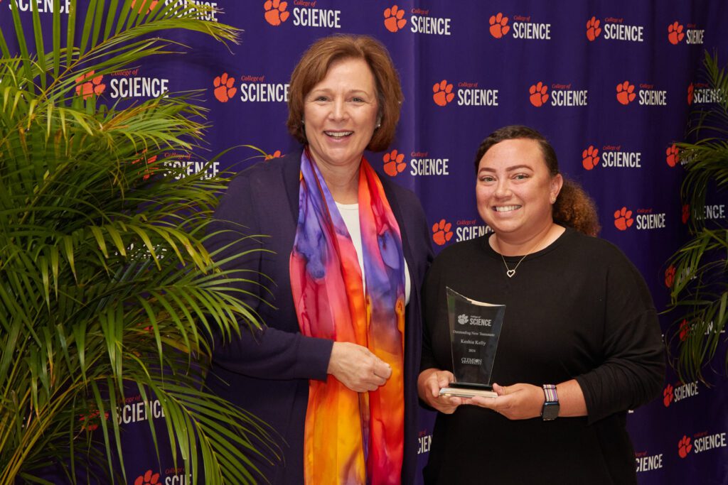 Two women holding a trophy stand in front of a College of Science backdrop.