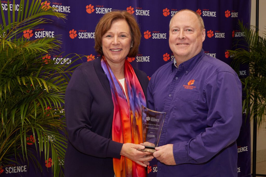 A woman and a man standing in front of a. College of Science backdrop next to a plant with one holding a trophy