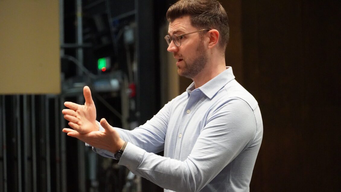 A man in a light blue dress shirt is animated as he teaches students.