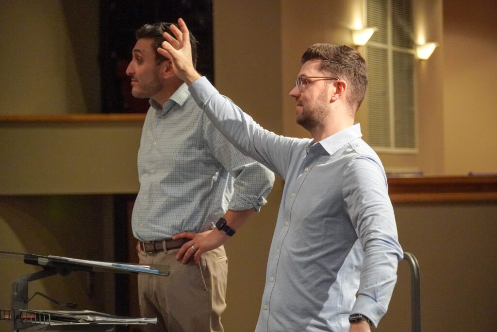 A man holds up his left hand while teaching.