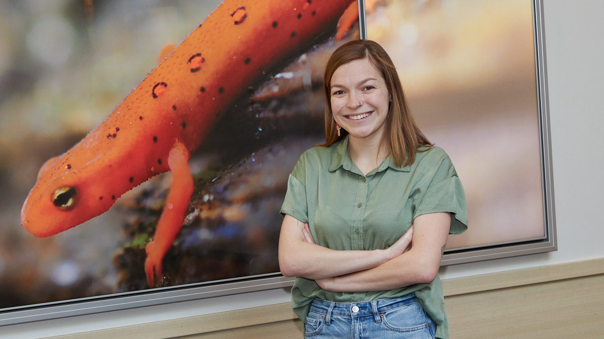 Woman wearing green shirt stands in front of a big photo of a salamander.