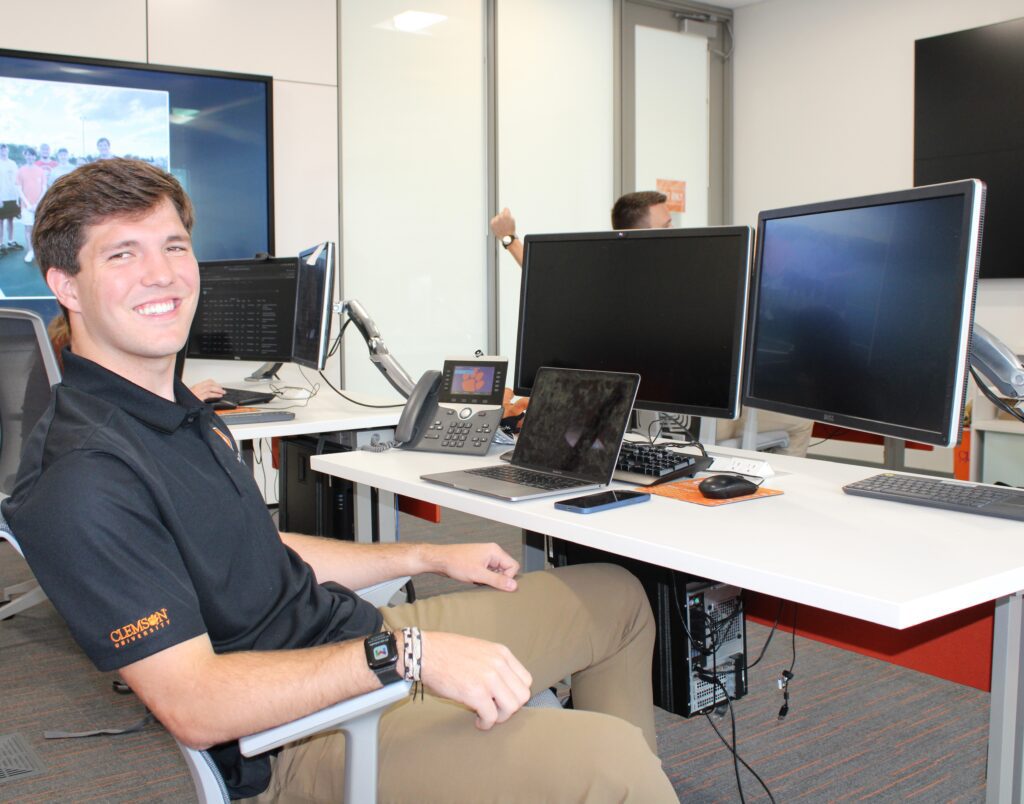 Student Levi Leard sits in front of a desk with two monitors and smiles.