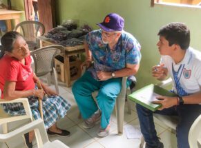 A man wearing scrubs and a Clemson Tigers hat talks to a Honduran woman while another man looks on.