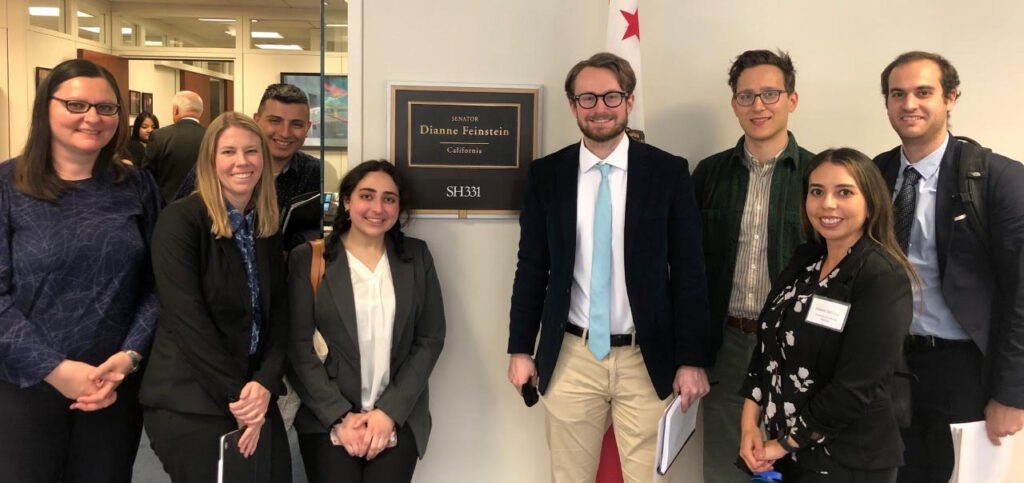 A group of people standing in front of a sign for Diane Feinstein's office at Capitol Hill