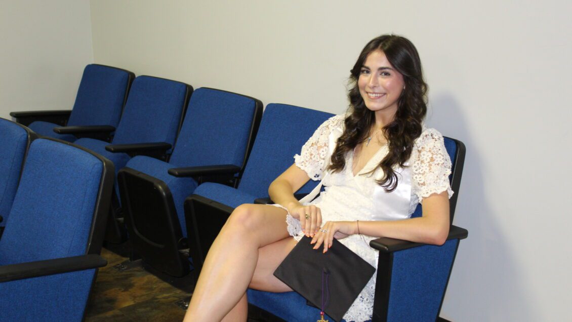 Sydney Olsen sits in McKissick Theater with a mortarboard in her hand.