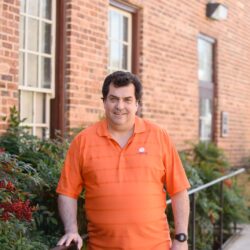 Man standing outside of a brick building while holding on stair railing.