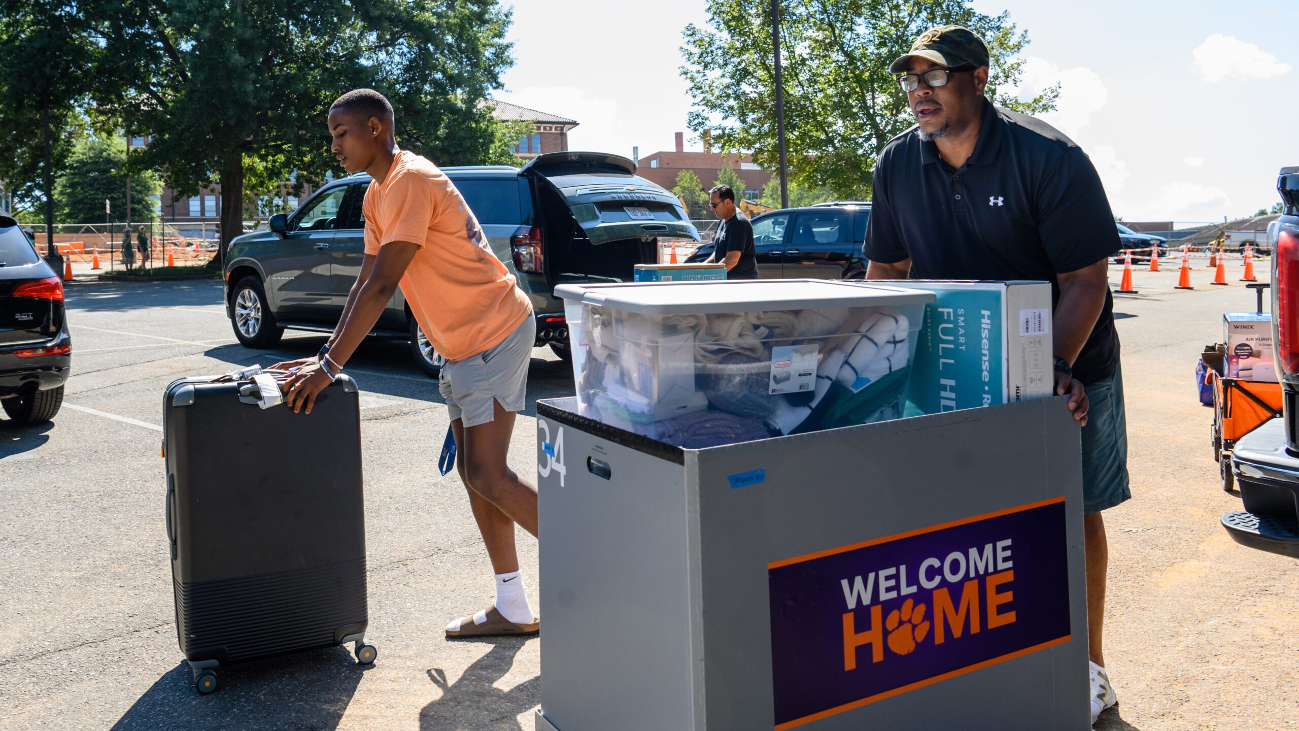 A father and son wheel dorm essentials and luggage through a parking lot.