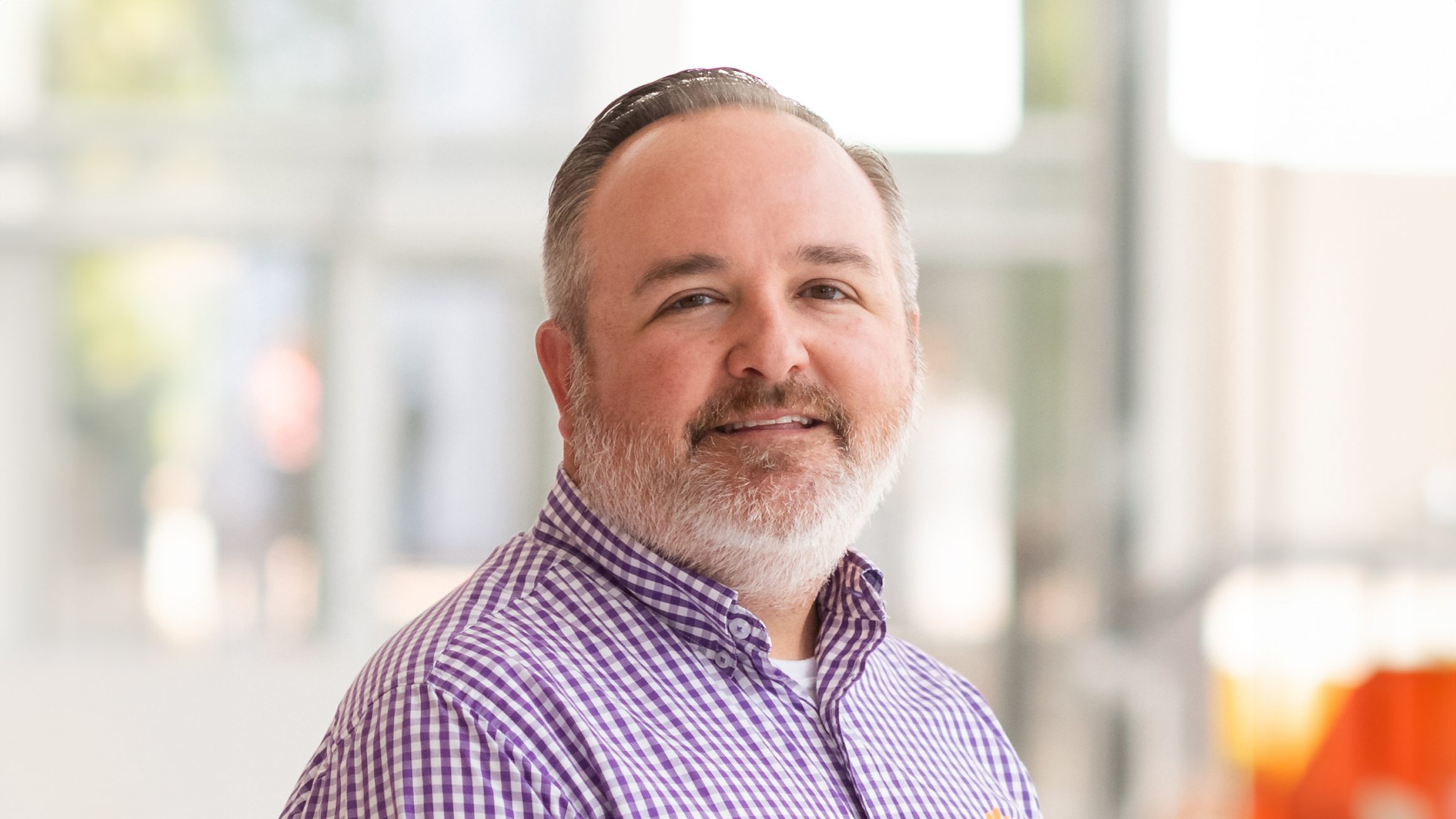 A man in a checkered purple and white shirt smiles.