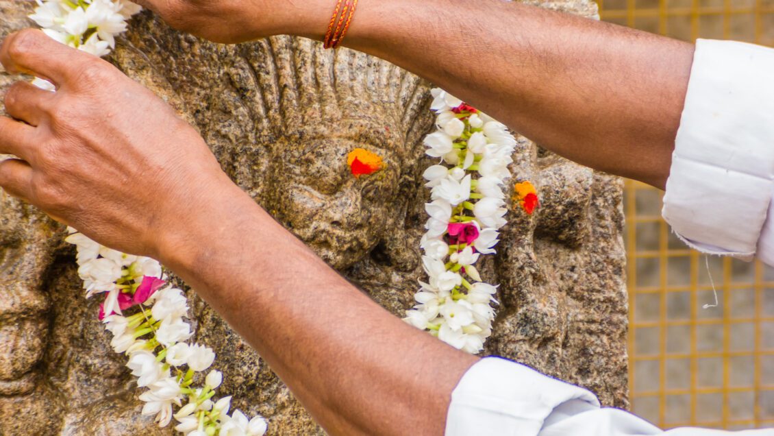 A Hindu offers a flowered garland to a god carved on a stone pillar at the the temple of Shiva in Nanjangud, South India.