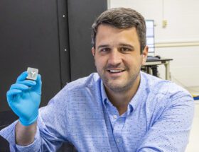 Man wearing a blue dress shirt and blue latex gloves holds a sample in a lab