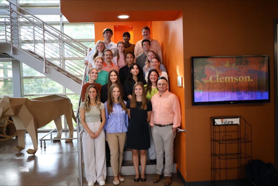 A group of students standing on steps with paper cow to the left and Clemson sign to the right.