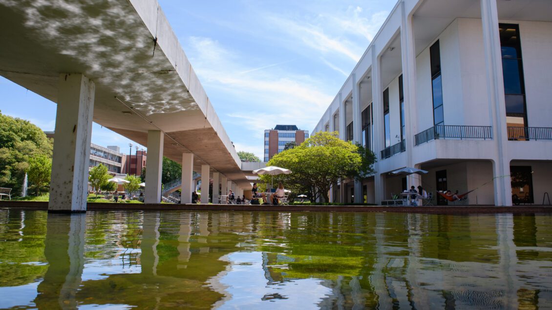 The Reflection Pond shimmers on the Cooper Library Bridge with students sitting at a table in the background.