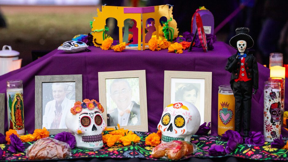 An altar used during a Day of the Dead celebration displaying photos of passed family members, decorated skulls, candles, and food.