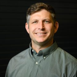 Portrait of a Caucasian man (James Sternberg) with short hair, parted on the side. He is smiling and wearing a button-down oxford shirt