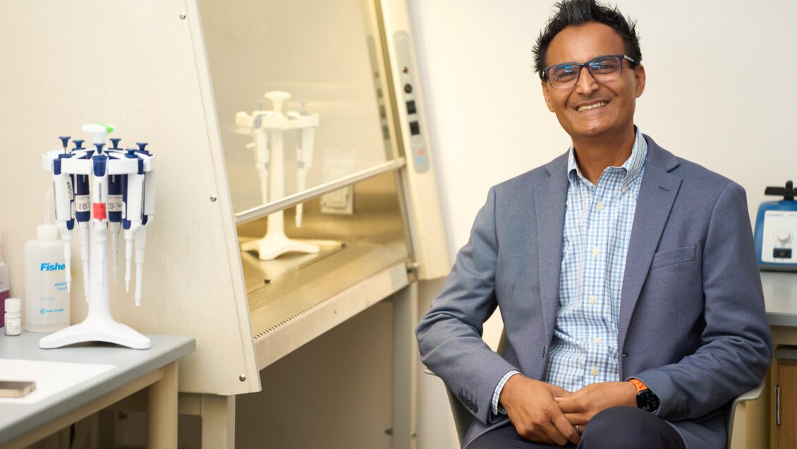 man wearing a suit coat sitting in a chair next to a hood in a science lab