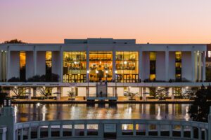 Campus at dusk shows the Cooper library's facade with the lights reflecting in a pond the foreground.