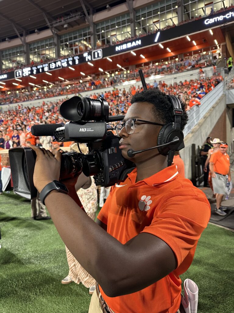 Xach Goldsmith holds a camera on the sideline of a Clemson football game