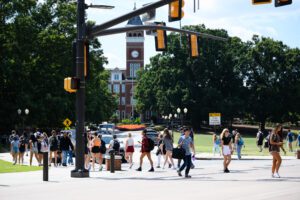 A diverse crowd of students crossing the road at a traffic light on a fall day, and Old Main is in the background.