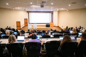 Large team of professionals in a classroom setting during a presentation.