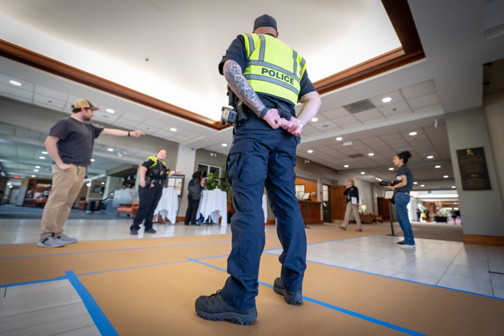 A police officer stands in the foyer of a hotel with his back to the camera as other officers talk around him