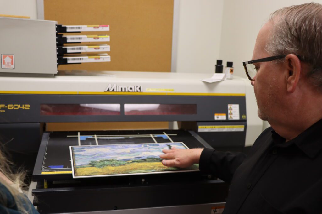 Carl Blue, associate professor of graphic communications, shows Dean York the process he went through to create his AI showcase.