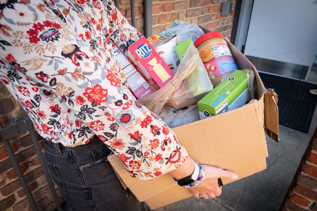 A person holds a cardboard box full of donated food items.