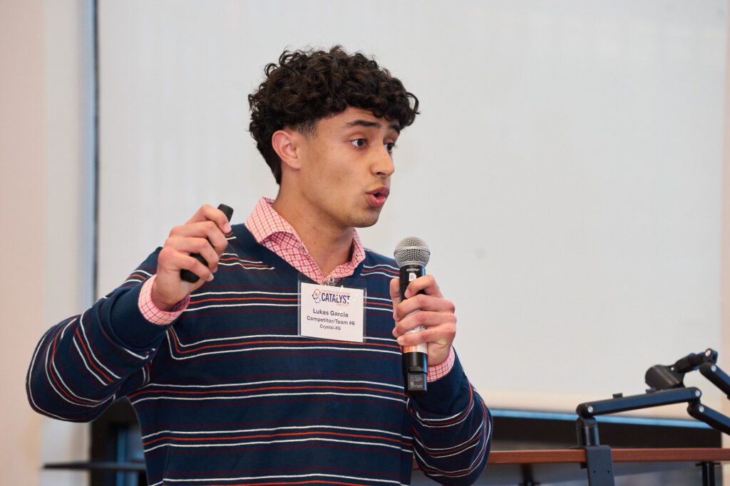 A student wearing a collared shirt and sweater holding a microphone during the College of Science's Catalyst Competition.