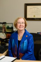 Woman wearing blue jacket and scarf sitting at a desk