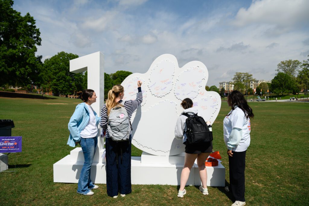 Four students are in the process of signing the six foot tall statue of a one and the Tiger Paw that represents 10.