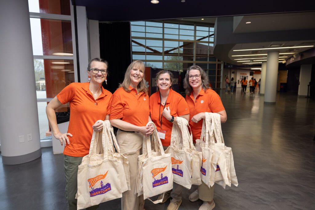 Clemson employees wearing orange polos hold "Tigertown Bound" tote bags.