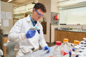 Man wearing a blue and red plaid shirt with white lab coat is pipetting