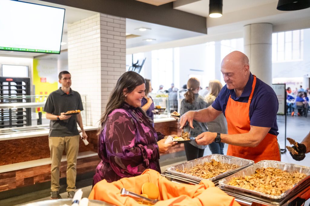 President Clements serves barbecue onto an employee's plate in a buffet line.