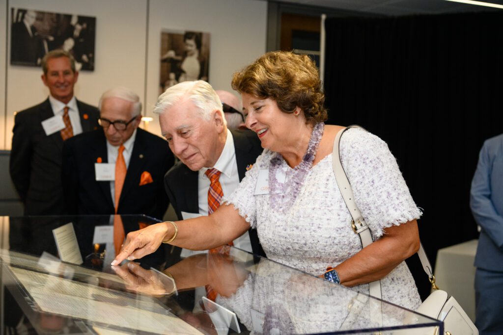 An older man and woman peer into a display case, the woman pointing at the documents inside.