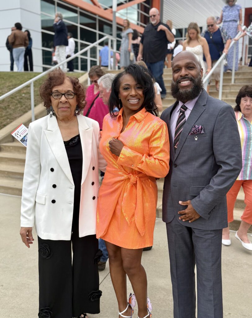 An African American woman stands between her parents as they all smile for a photograph.