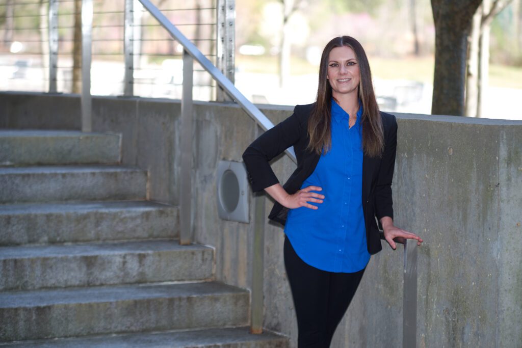 Woman wearing black suit and blue shirt leans against a rail near some steps.