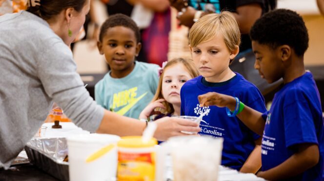 Elementary school students conduct a science experiment at a booth.