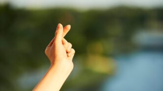Hand of young woman making heart gesture with her fingers against blurred landscape