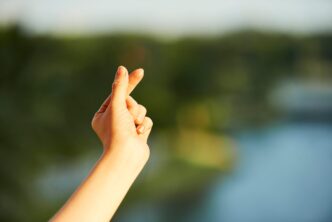 Hand of young woman making heart gesture with her fingers against blurred landscape