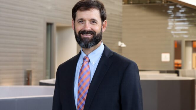 Brandon Lockhart, chair of the department of finance. He, a white man with brown hair and a brown beard, stands center frame smiling at the camera.