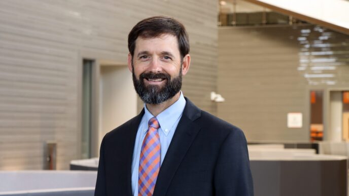 Brandon Lockhart, chair of the department of finance. He, a white man with brown hair and a brown beard, stands center frame smiling at the camera.