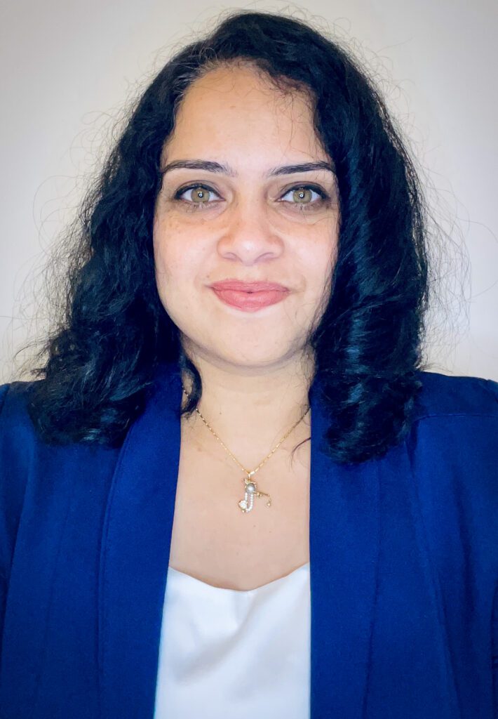 A headshot of a woman with dark hair wearing a blue sport coat and silk shirt smiling at the camera.