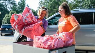 A woman helping a student move bags into a residence hall.