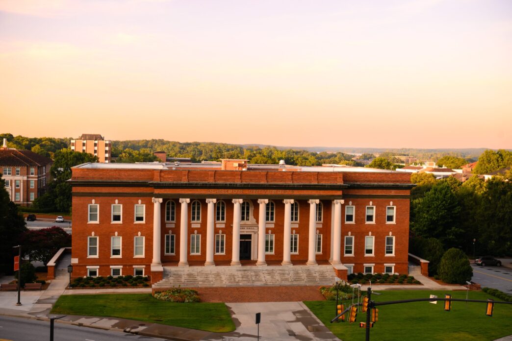 The front of Sikes Hall with the sunrise in the background.