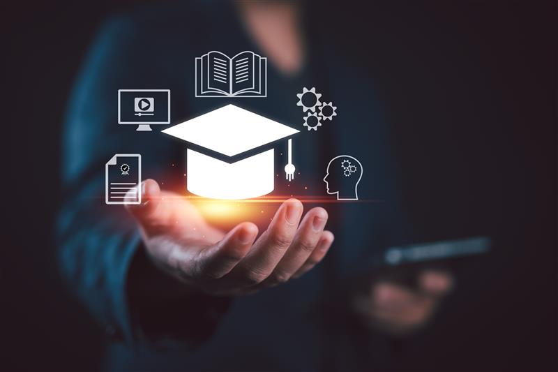 An artist illustration showing a hand with a graduation cap and a book, a computer screen, and a brain to represent an AI-assisted virtual teaching assistant.