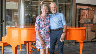 Bill and Donna Eskridge pose in front of the Clemson Orange Steinway Piano