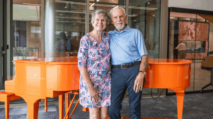 Bill and Donna Eskridge pose in front of the Clemson Orange Steinway Piano